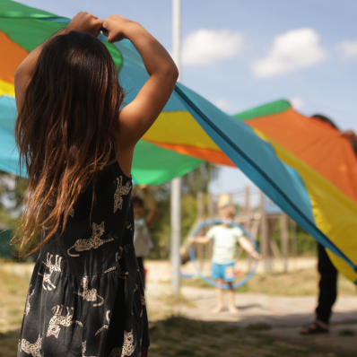 Auf dem Bild ist ein Kind von hinten zu sehen, welches ein großes Tuch mit anderen Kindern festhält.